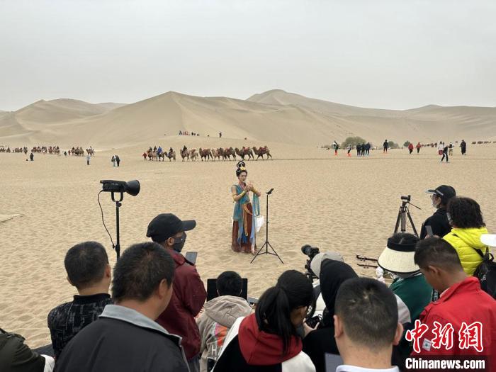 圖為2023年4月底，敦煌大漠“逐舞者”奧楠在鳴沙山月牙泉景區(qū)視頻直播，吸引游人圍觀?！●T志軍 攝